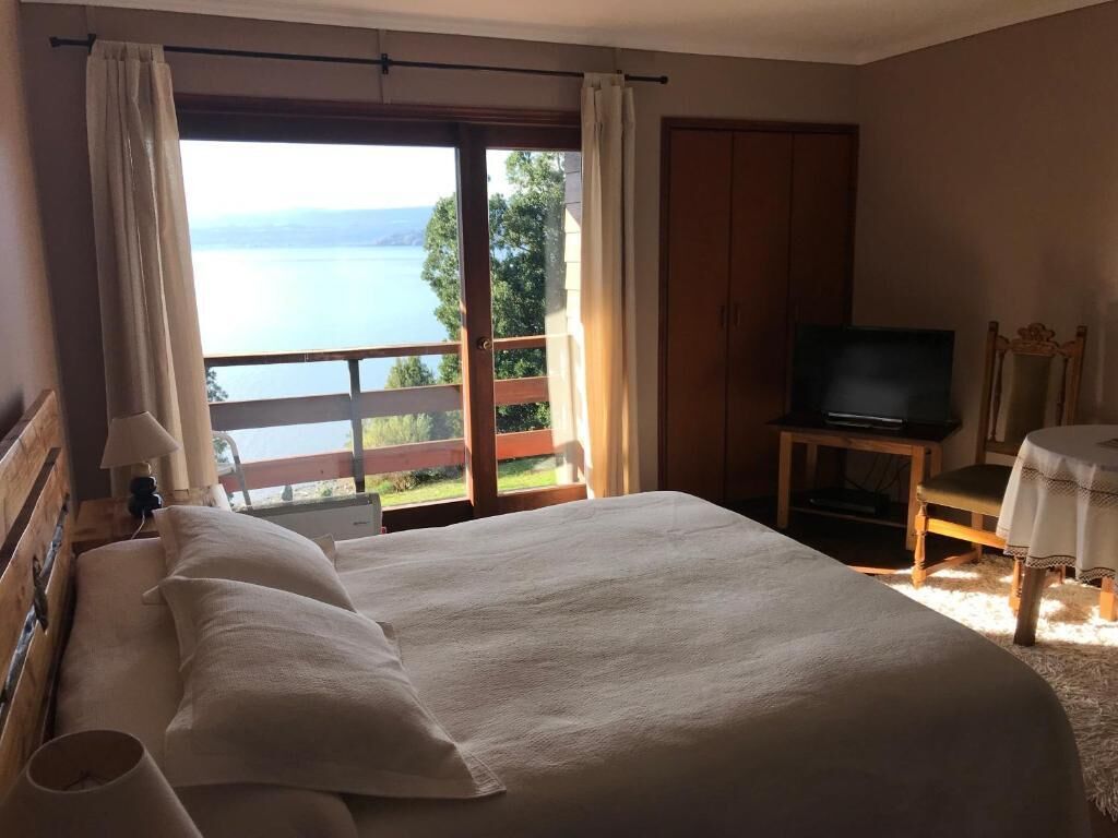 Una camera da letto con un grande letto, una televisione su un mobile in legno e vista su un lago attraverso una porta scorrevole.