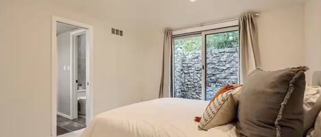 A bedroom with a bed, a window with curtains, and a view of a stone wall outside.