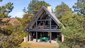 Une cabane moderne, de forme triangulaire, dotée d’un balcon et entourée de pins.