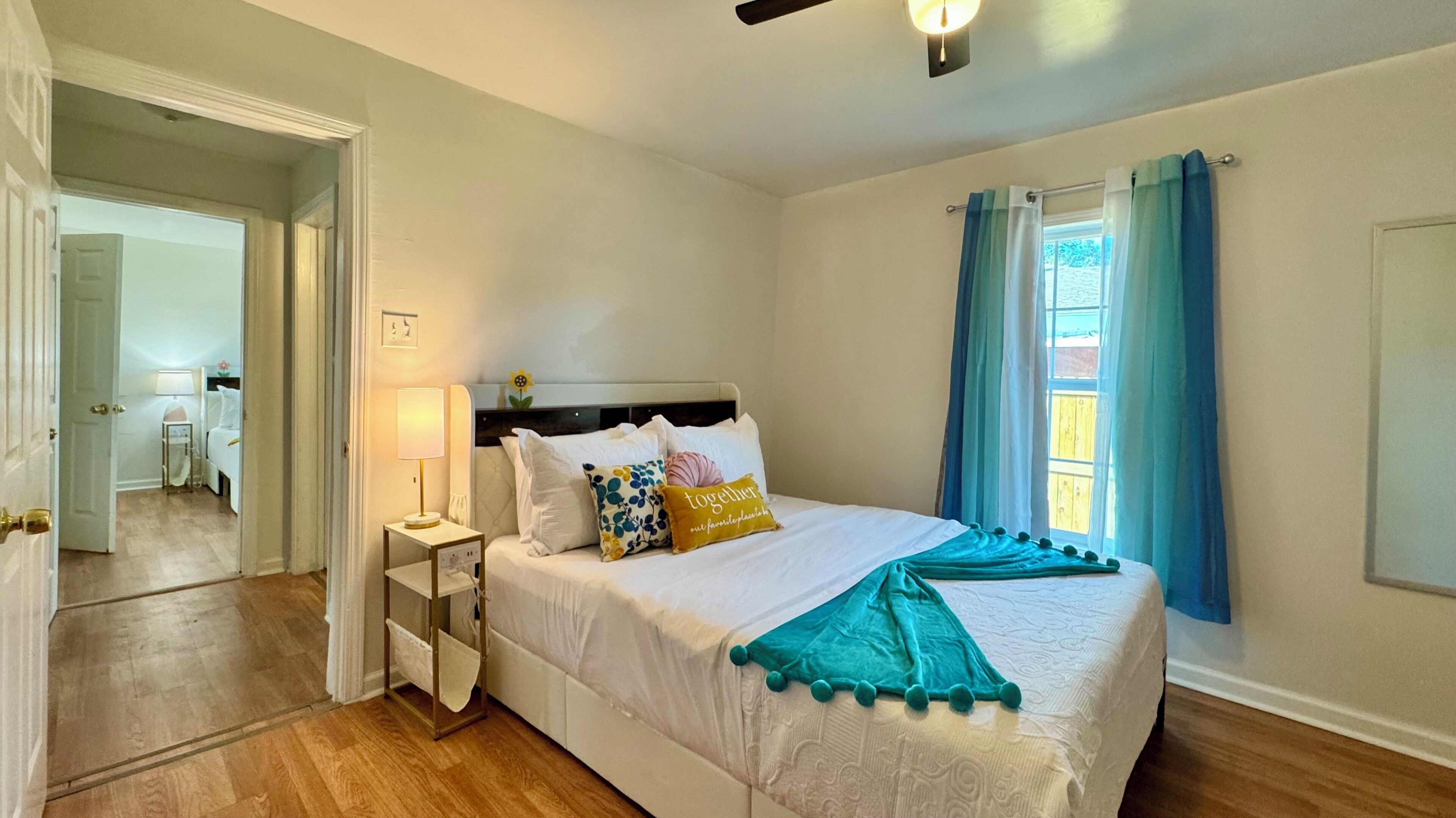 Un dormitorio ordenado con cama, mesitas de noche, una lámpara y una ventana con cortinas.