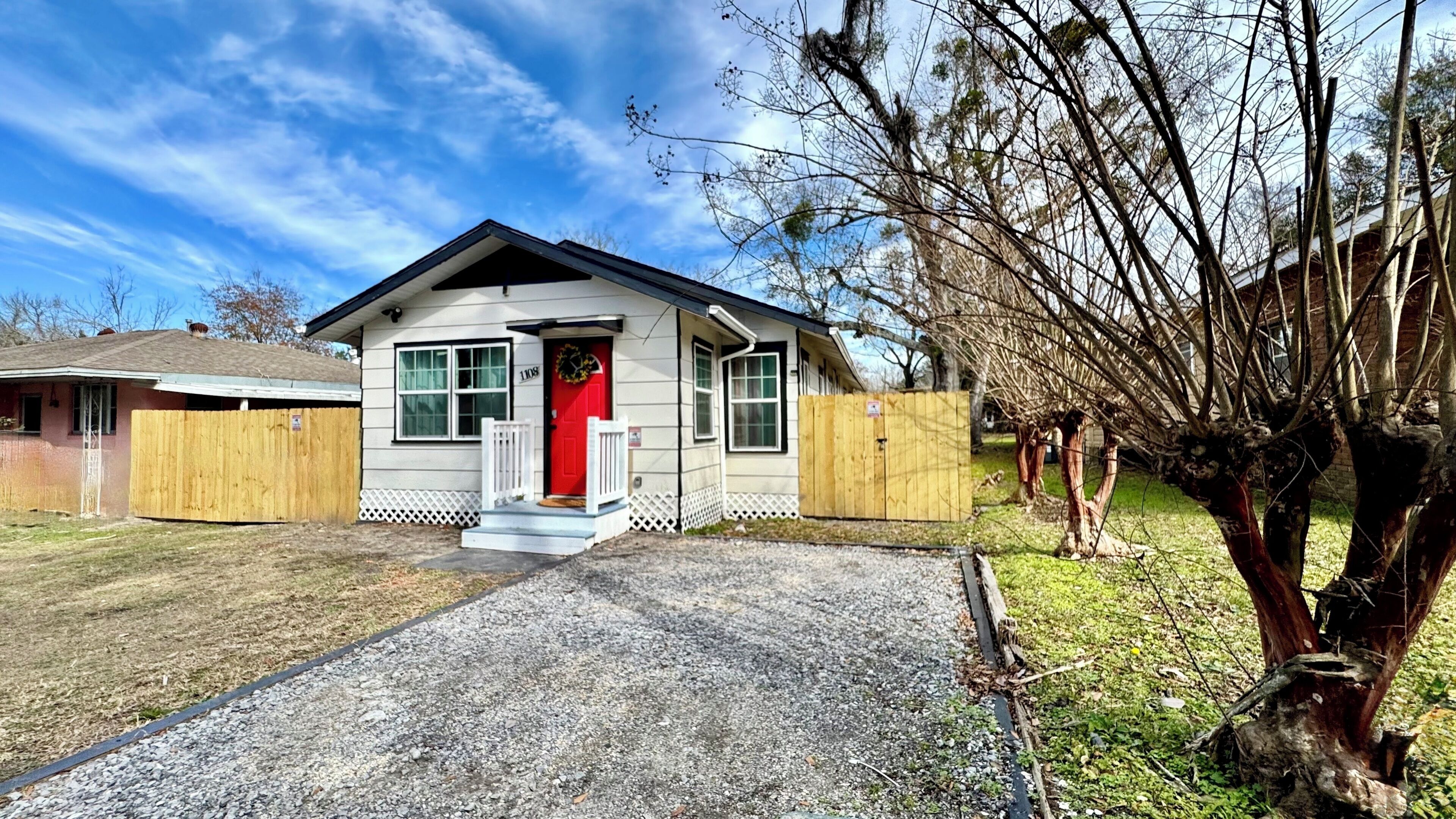 A single-story house with a red door, a front porch, and a gravel driveway.