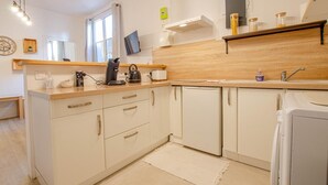 A compact kitchen with white cabinets, a wooden countertop, a coffee maker, a kettle, and a dishwasher. - L'Idylle - SAINTE SAVINE (SAINTE SAVINE)
