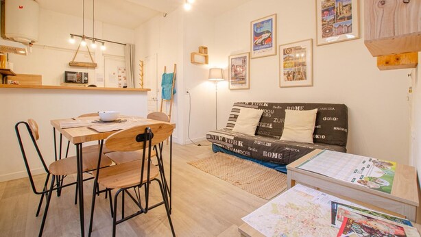A cozy living room with a sofa bed, a dining table with chairs, a kitchen area with a microwave, and various framed pictures on the walls. - L'Idylle - SAINTE SAVINE (SAINTE SAVINE)