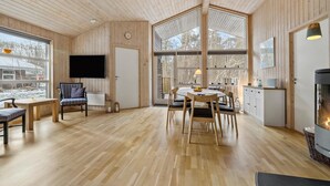 A spacious room with wooden floors, a dining table with chairs, a television mounted on the wall, and a fireplace.