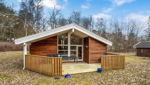 A wooden cabin with a porch, large windows, and a fenced deck area.