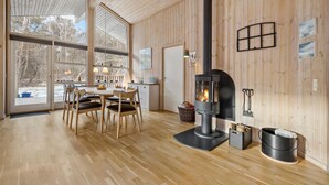 A wooden interior with a central fireplace, a dining area, and large windows.