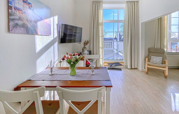 A dining area with a wooden table, white chairs, a vase with flowers, and a TV on the wall.