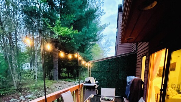 Una terrazza esterna con un tavolo e sedie in vetro, circondata da una ringhiera in legno e un tappeto decorato.