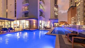 An indoor swimming pool with multiple lanes, surrounded by lounge chairs and a poolside area with a view of tall buildings. - Great Value CBD 2 Beds Apt Free Carpark/ Pool /Gym (Brisbane City)