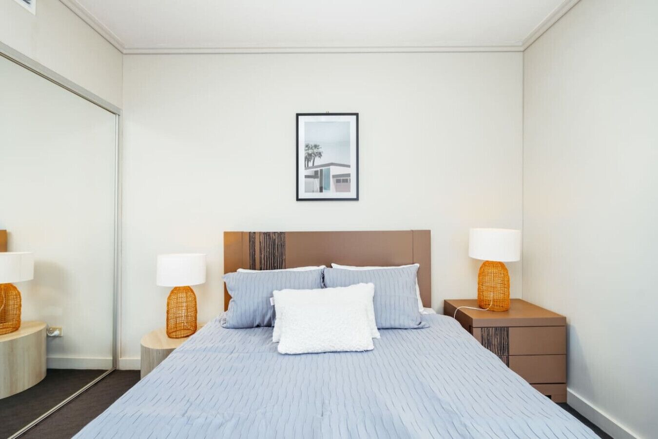 Un cuarto de hotel ordenado con una cama grande, dos mesitas de noche con lámparas y un cuadro en la pared.