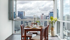 A dining area with a table set for four, a potted plant, and a city view through large windows. - Great Value CBD 2 Beds Apt Free Carpark/ Pool /Gym (Brisbane City)