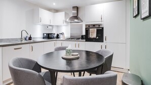 Una cocina moderna con armarios blancos, una mesa redonda de comedor con cuatro sillas y una estufa a gas.