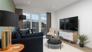 Una sala de estar moderna con sofá, mesa de centro, televisor y lámpara.