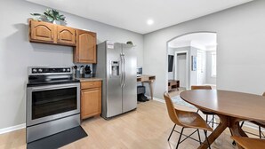 A modern kitchen with stainless steel appliances, wooden cabinets, and a dining area with a round table and chairs. - Spacious Mid Century Modern 1 Bed 1 Bath 65" TV (Wyandotte)