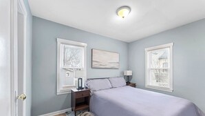 A bedroom with a bed, nightstands, a lamp, and a painting on the wall. - Spacious Mid Century Modern 1 Bed 1 Bath 65" TV (Wyandotte)