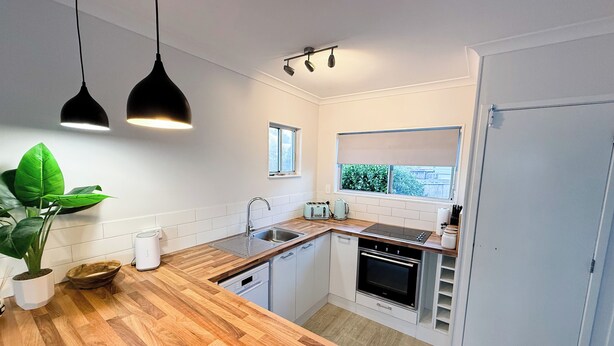A compact kitchen with a wooden countertop, a sink, a toaster, and a window with a view of greenery. - Cozy unit Papamoa Beach (Bay of Plenty)