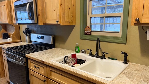 A kitchen with wooden cabinets, a stainless steel stove, a sink, and a window with a view of trees.