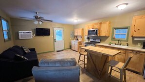 A compact living space with a kitchenette, a ceiling fan, a TV, and a sofa.