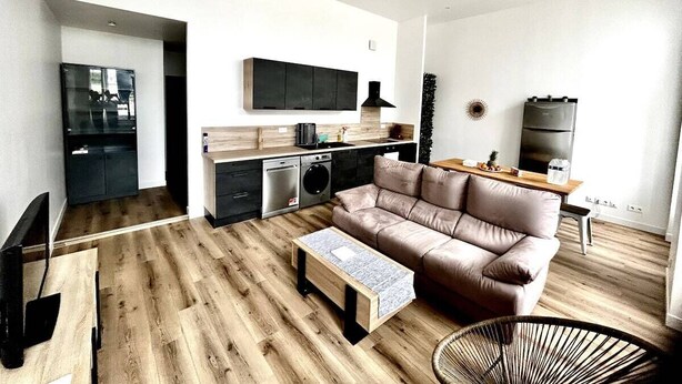 A modern living room with a sofa, coffee table, and a dining area with a TV and kitchen appliances.