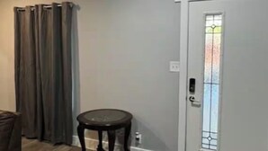 Een kamer met een grijze muur, een witte deur met een ruitpaneel, een ronde houten tafel en een bruine lederen stoel.