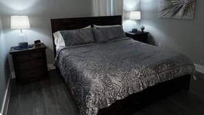 Een slaapkamer met een bed, twee nachtkastjes, een lamp, een gordijn en een wanddecoratie.