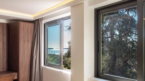 A room with a large window, a view of the sea, and a wooden cabinet.