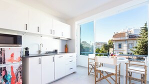 A modern kitchen with white cabinets, a large window, and a view of buildings.