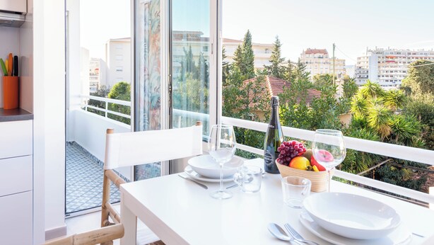 A balcony with a dining table set for two, a bottle of wine, and a bowl of fruit.
