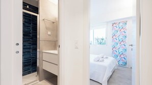 A hotel room with a walk-in closet, a bed with a white bedspread, and a window with a view of buildings.