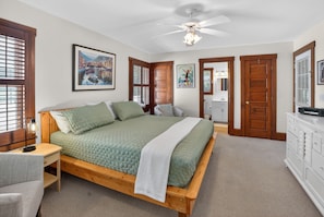 Um quarto com uma cama de madeira, uma mesa de cabeceira, uma escrivaninha, uma cadeira, um ventilador de teto e um armário.