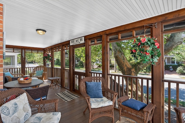 A covered porch with wicker furniture, a sign reading 'BEACH,' and a hanging basket with flowers.