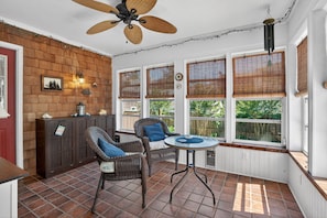 A sunroom with wicker furniture, a ceiling fan, and large windows with blinds.