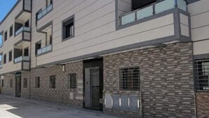 Un edifici modern de diversos pisos amb balcons, façana de pedra i cel blau.