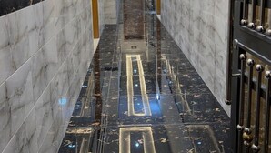 Passadís amb sòl de marbre, il·luminació encastrada i una reixa metàl·lica a la dreta.