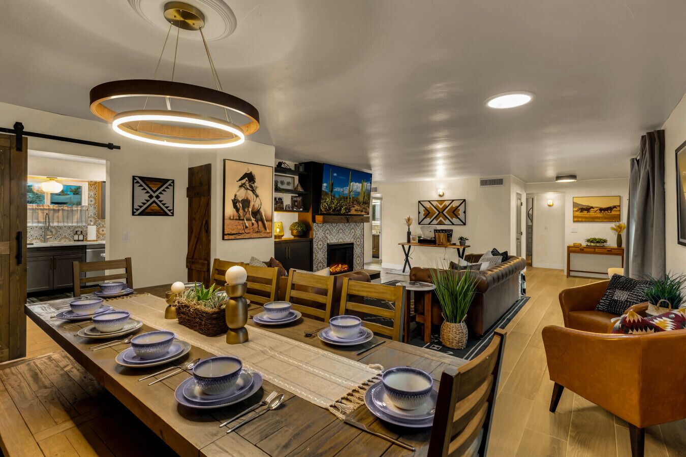 A modern dining area with a long wooden table set for a meal, a fireplace, and a cozy seating area with a sofa and armchairs.