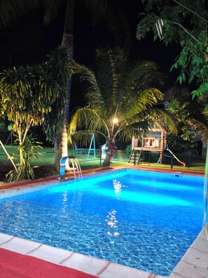 A swimming pool with clear blue water, surrounded by palm trees and a wooden play structure. - Fully equipped cabins for up to 6 people. Surrounded by nature.  (Puerto Iguazú)