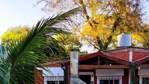 A brick house with a chimney, a patio with chairs, and a large tree.
