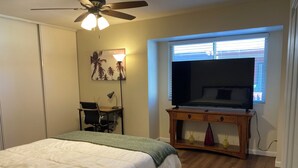 Une chambre à coucher comprenant un lit, un bureau, une chaise, un téléviseur et une fenêtre avec des stores.