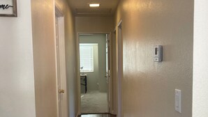 Un couloir étroit avec un plancher en bois, des murs blancs et un luminaire au plafond.