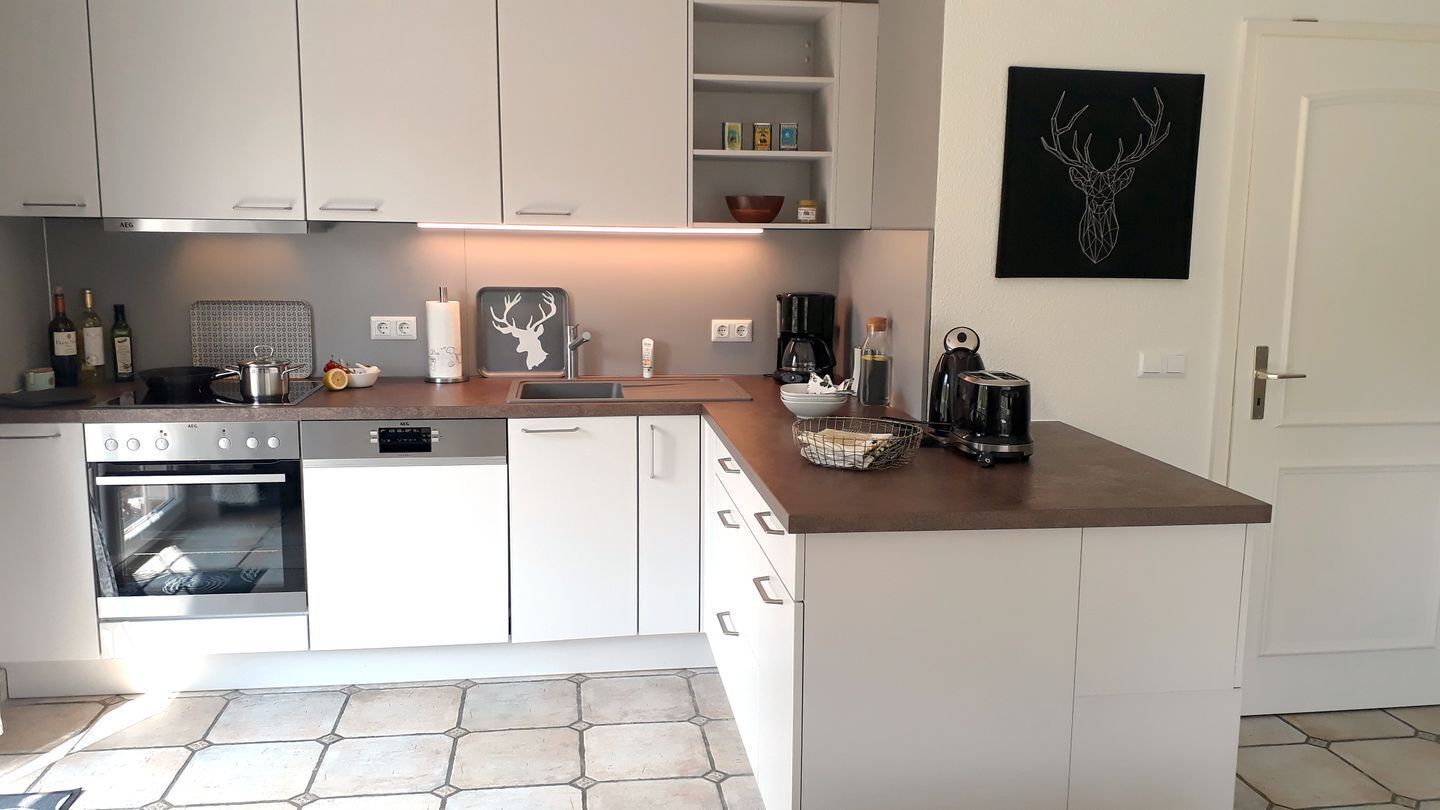 Una cocina moderna con gabinetes blancos, horno integrado, cafetera y un cuadro con la imagen de un ciervo en la pared.