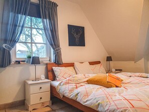 Un dormitorio con cama, mesitas de noche, una ventana con cortinas, una obra de arte en la pared y una lámpara.