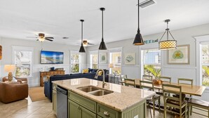 A spacious kitchen with a central island, pendant lighting, and a dining area with wooden chairs and a table. - Nautical Tides: 3 Blocks to Beach! Pool Spa! Rooftop Deck by Anna Maria Life Vacation Rentals (Bradenton Beach)