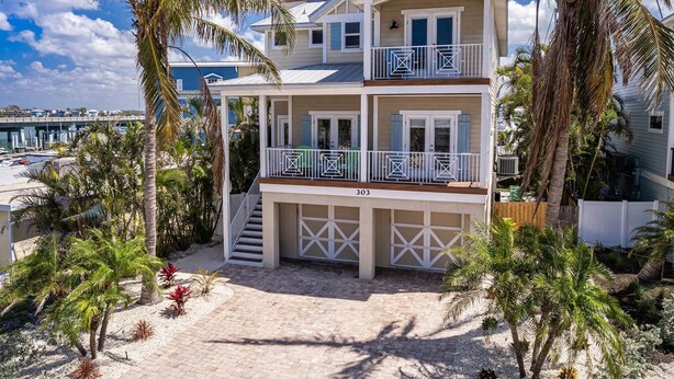 A two-story beachfront house with a balcony, a garage, and a view of the beach and ocean. - Nautical Tides: 3 Blocks to Beach! Pool Spa! Rooftop Deck by Anna Maria Life Vacation Rentals (Bradenton Beach)