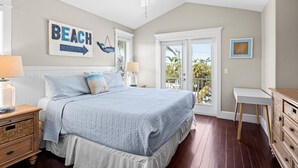 A bedroom with a bed, a nightstand, a dresser, a ceiling fan, and a view of the outdoors. - Nautical Tides: 3 Blocks to Beach! Pool Spa! Rooftop Deck by Anna Maria Life Vacation Rentals (Bradenton Beach)