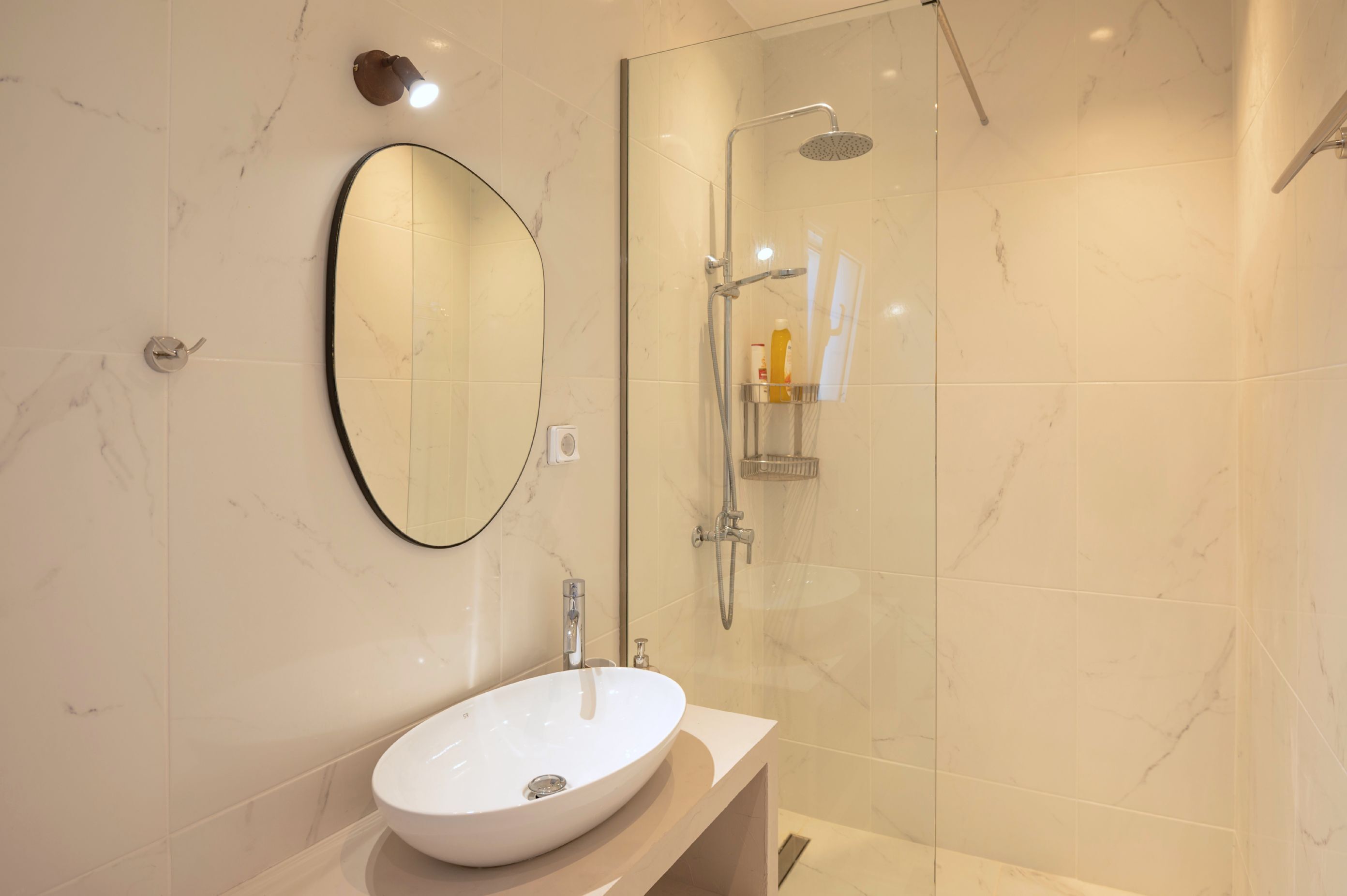 Un baño moderno con un lavamanos ovalado grande, un espejo y una zona de ducha con mampara de cristal.