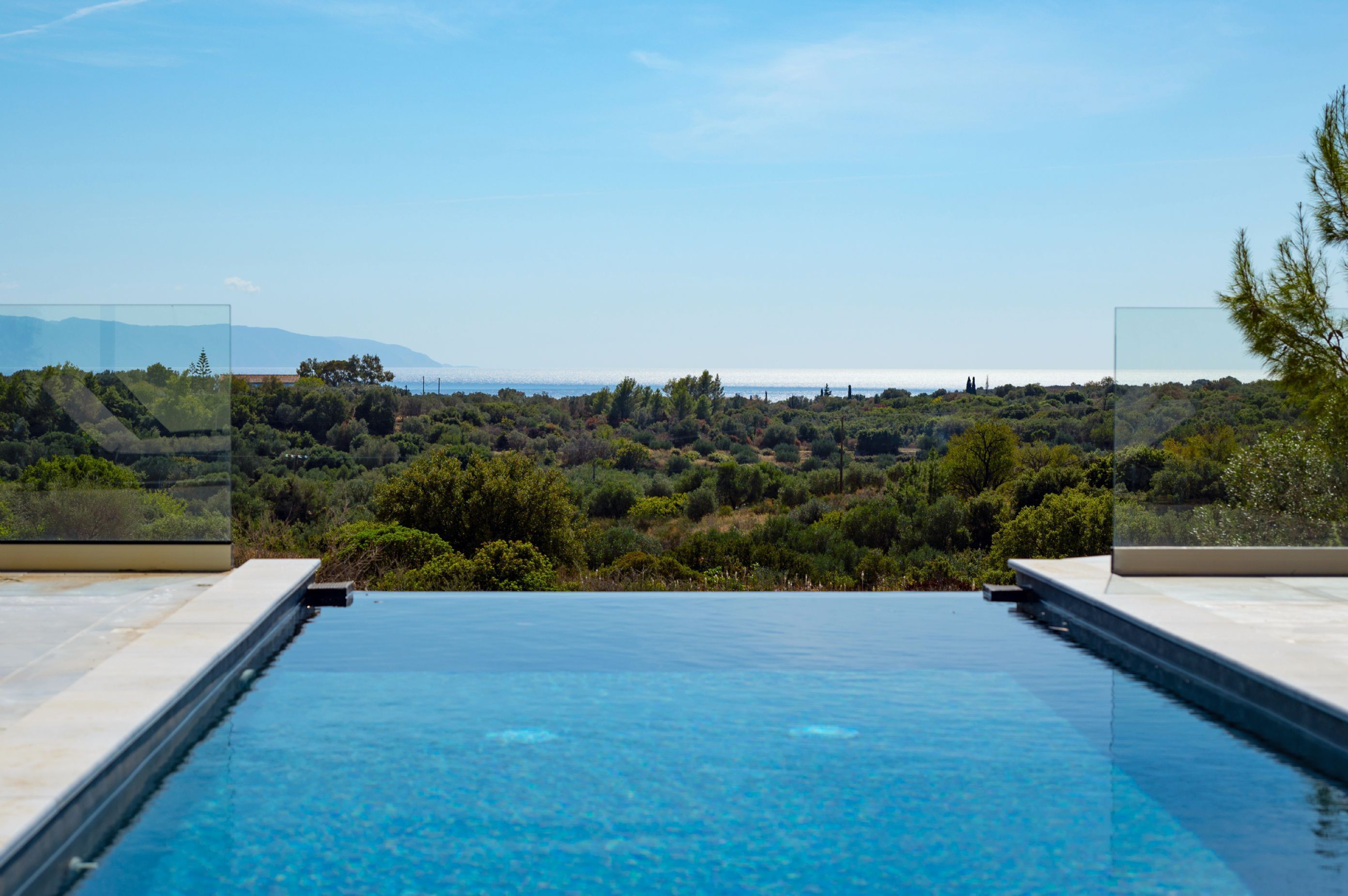 A clear blue infinity pool with a view of a lush landscape and distant mountains.