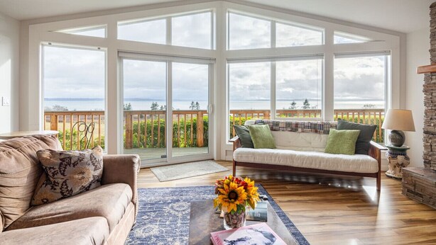 Een ruime woonkamer met een grote schuifpui die leidt naar een balkon met uitzicht op zee.