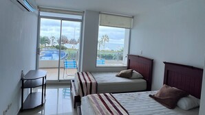 Une chambre d’hôtel avec deux lits, un bureau et de grandes fenêtres donnant sur une piscine et des palmiers.