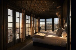 A bedroom with a large bed, multiple windows, and a view of the landscape.