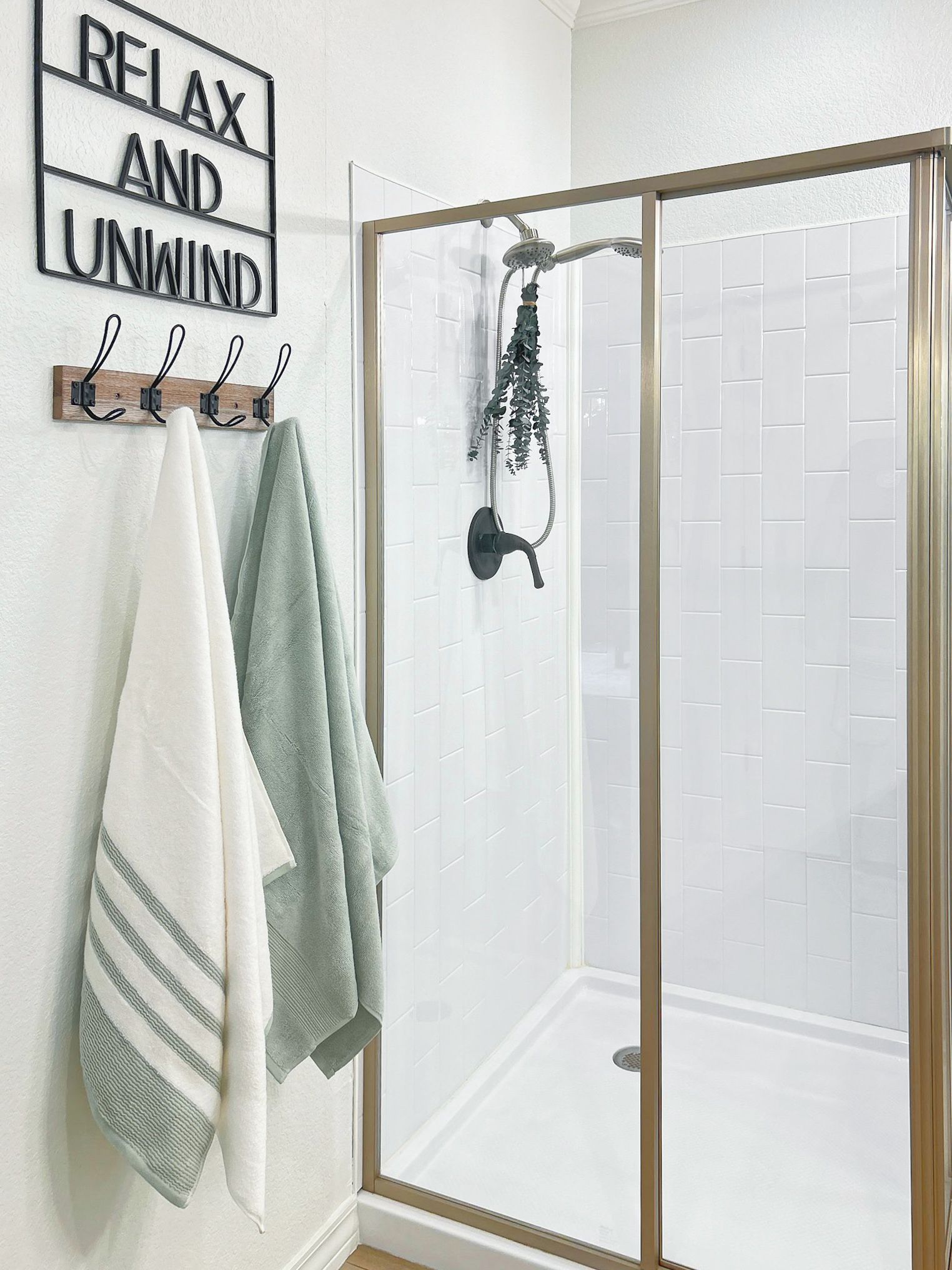 A bathroom with a glass shower enclosure, white tiled walls, and a towel rack with three towels.
